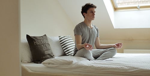 Young Man Meditating with Earbuds on Bed