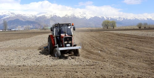 Red Tractor Plowing Field in Rural Mountain Setting
