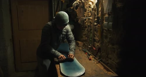 Man starts scraping of wax of a snowboard. Inside a mountain shed. Zillertal, Austria