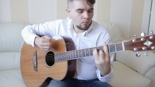 Young Adult Plays Acoustic Guitar on Couch