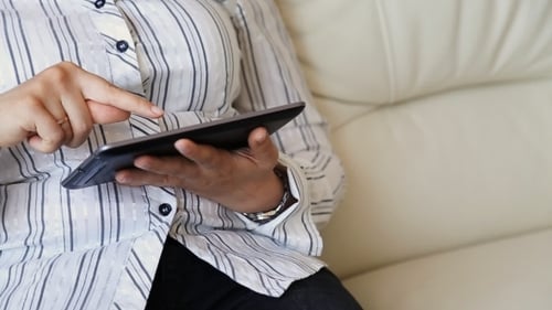 Adult Uses Tablet While Sitting on Couch Indoors