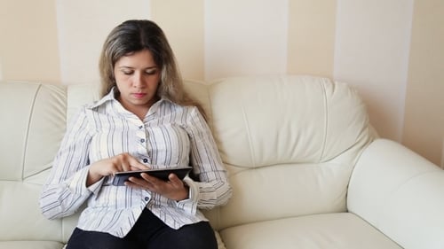 Woman Using Tablet Computer Sitting on Couch Indoors