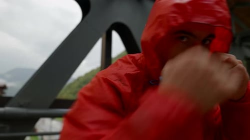 Man in Red Raincoat Boxing Outdoors on Bridge
