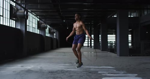 Shirtless african american man skipping the rope in an empty urban building