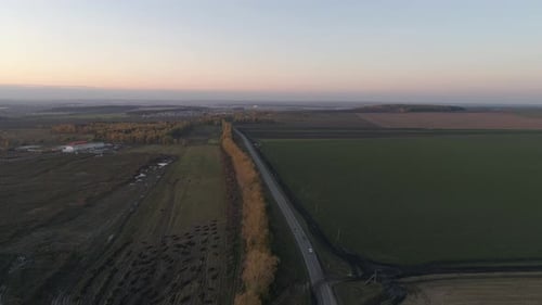 Die Straße zwischen den Feldern. Fahr ein Auto. Abend. Schwenken geschossen. Luftbild