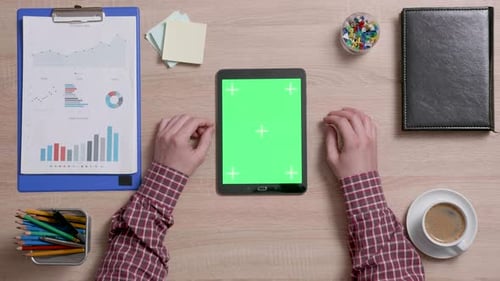 Top View of Male Using Both Hands to Zoom in a Green Screen on a Black Tablet