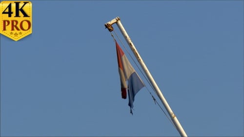 Tattered Flag Hangs on Pole Under Blue Sky