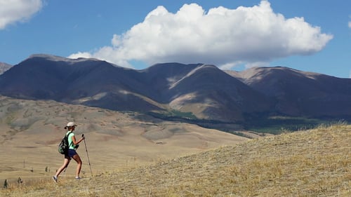 Woman Hikes Up Grassy Hill in Mountain Landscape