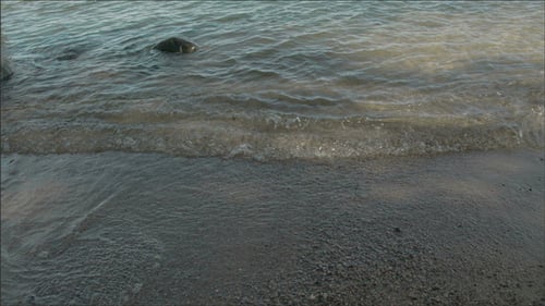 Waves Gently Lapping Rocky Beach Shoreline on Sunny Day