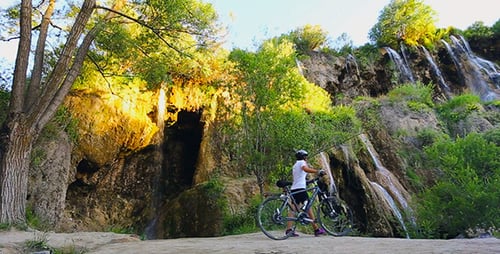 Cyclist Arrives at Waterfall with Bicycle