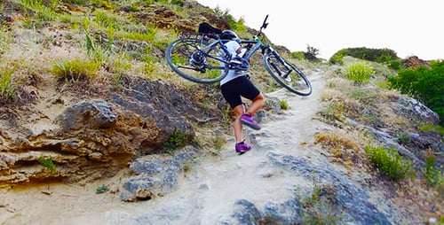 Woman Carries Bicycle Up Steep Hillside