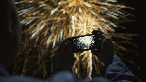 Person Recording Fireworks Display at Night with Smartphone