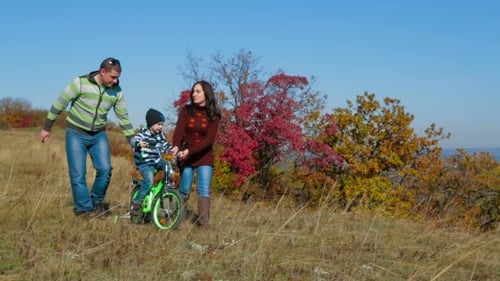 Family Walks as Child Rides Bicycle on Hillside