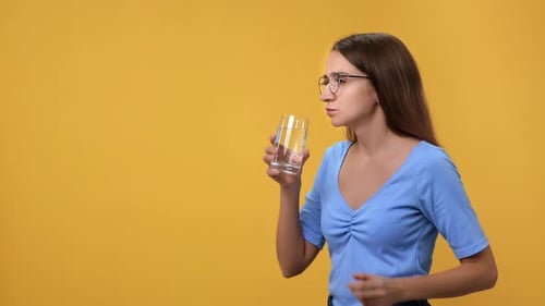 Woman Taking Pill with Water on Yellow Background
