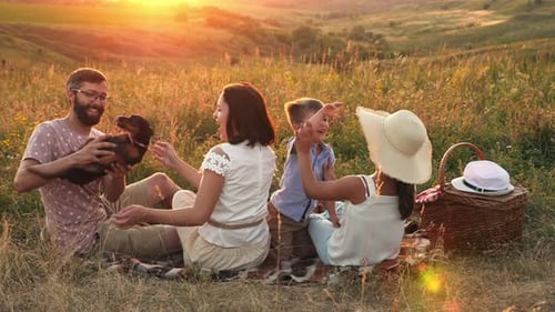 Family Picnic at Sunset with Dog in Grassy Field