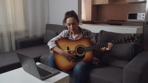 Woman plays guitar sitting on a couch