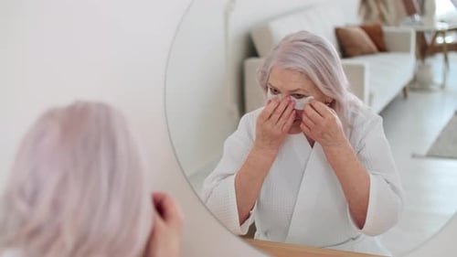 Senior Woman Applies Beauty Eye Patches in Mirror