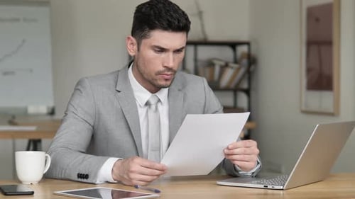 Thoughtful Young Adult at Desk Reading Documents