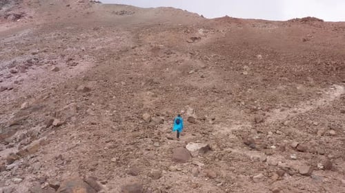 Woman or backpacker hiking up a slope with many loose rocks to reach the tope of the mountain