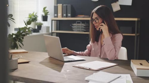 Businesswoman Talking on Phone and Using Laptop in Office