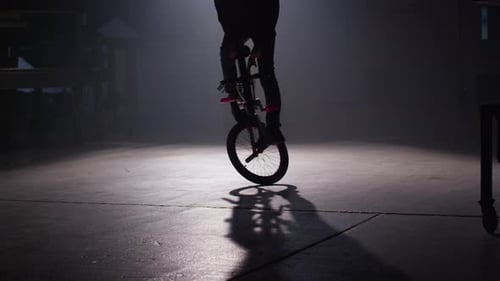 BMX rider doing tricks in dark warehouse.