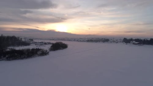 Aerial Orbital Shot of the Frozen Snow Covered Winding River Surrounded with a Little Village on a