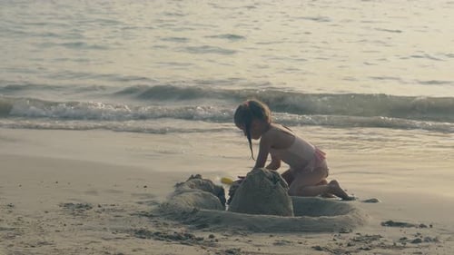 Linda chica con trenzas construye un castillo de arena en la playa nocturna