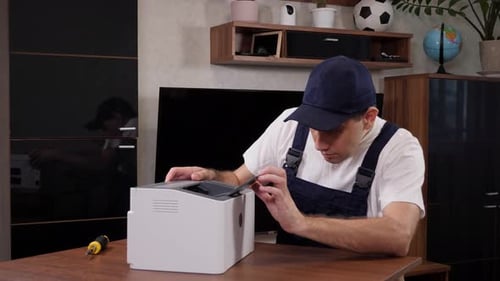 Ein männlicher Handwerker im blauen Overall inspiziert einen Drucker, bevor er mit Reparaturen beginnt