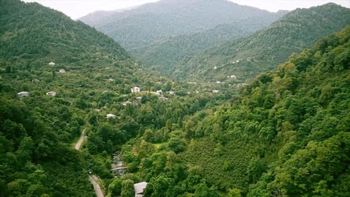 Aerial drone view of nature in Georgia. Valley with narrow river and village, hills slopes covered w