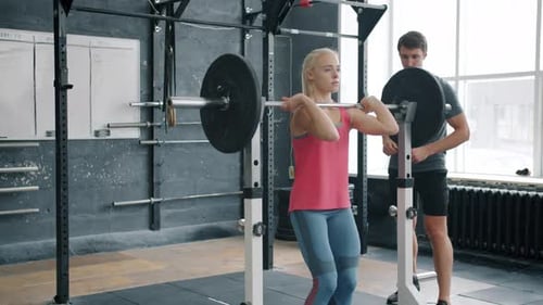 Slender Sportswoman in Sportswear Squatting with Barbell Working Out with Coach in Gym