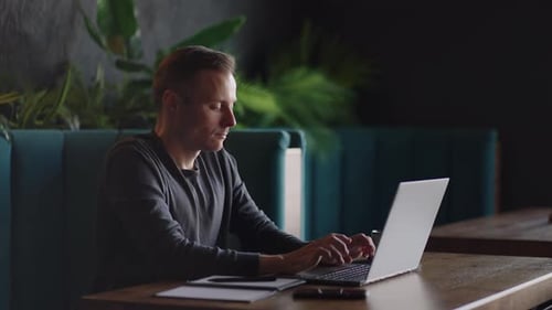 Handsome Freelancer Businessman in Glasses Diligently Working on Laptop in Cafe