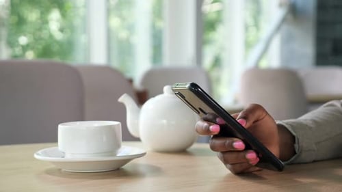 Black Woman Texts Message on Smartphone at Table in Cafe