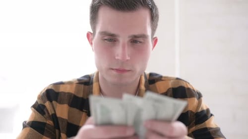 Jeune homme comptant le dollar papier-monnaie