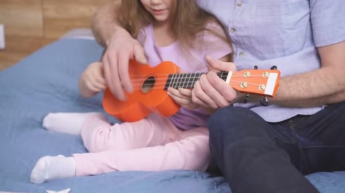 Child Learns Ukulele From Adult in Bedroom
