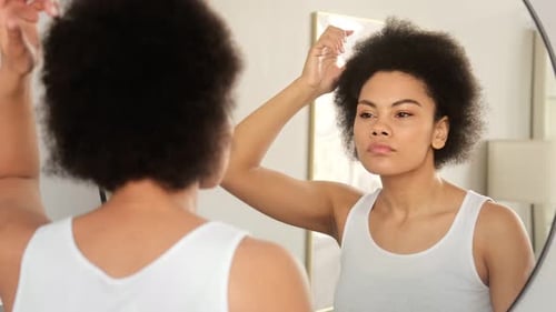 Young Woman Styles Black Hair in Mirror