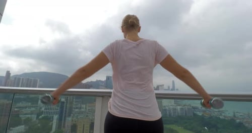 In Hong Kong, China on the terrace a young girl does exercises with dumbbells spreading hands