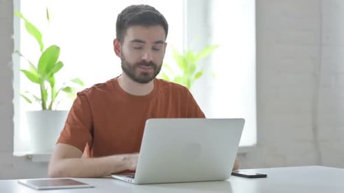 Young Man Working on Laptop at Home Gives Thumbs Up