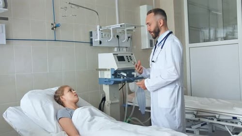 Doctor Standing Near Hospital Bed and Discussing with Young Female Patient
