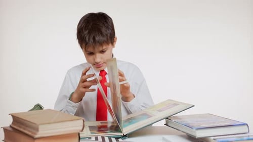 Curious School Kid in Red Tie Sitting at Table Folding Pages of Geographic Atlas with Interest on