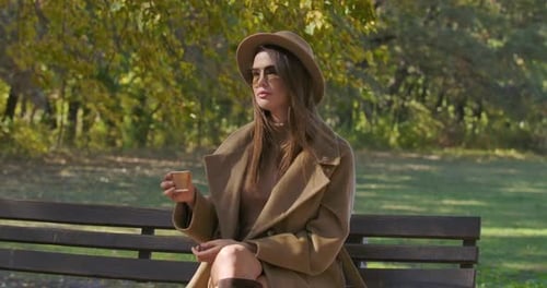 Stylish Woman Enjoys Coffee on Park Bench