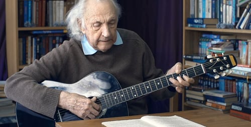 Senior Man Plays Guitar in Home Library