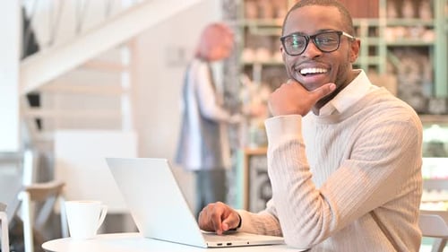 Cheerful Man with Laptop Smiling at Camera in Cafe