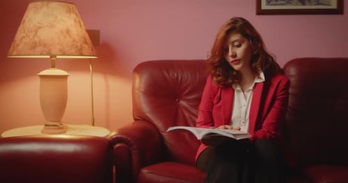 Woman Reads Book on Red Leather Couch