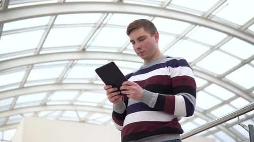 A Young Man Is Standing with a Tablet. A Man Uses a Tablet Against a Pan-glass Roof. A Busy Person