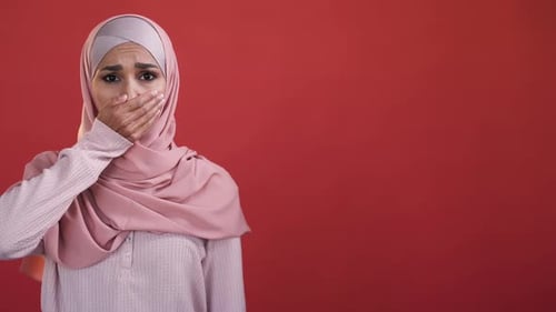 Woman in Headscarf Covers Mouth, Concerned Expression
