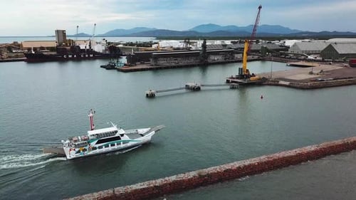 Drone moving foward showing vehicle barge cruising into harbour. Industrial port facilities can be s