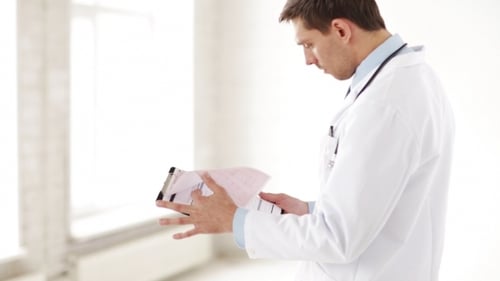 Male Doctor Reading Medical Documents At Hospital
