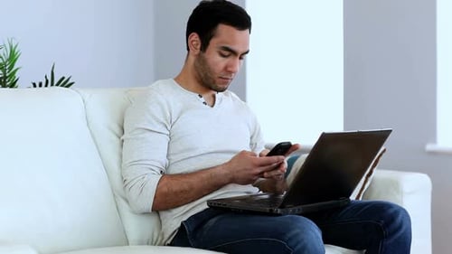 Man Relaxing on Couch with Phone and Laptop