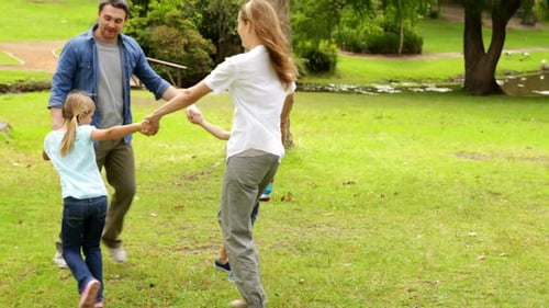 Happy Family Playing Ring A Rosie In The Park Together