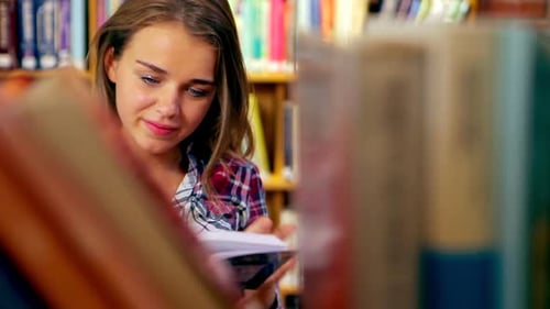 Glücklicher Student liest Buch im Stehen in der Bibliothek